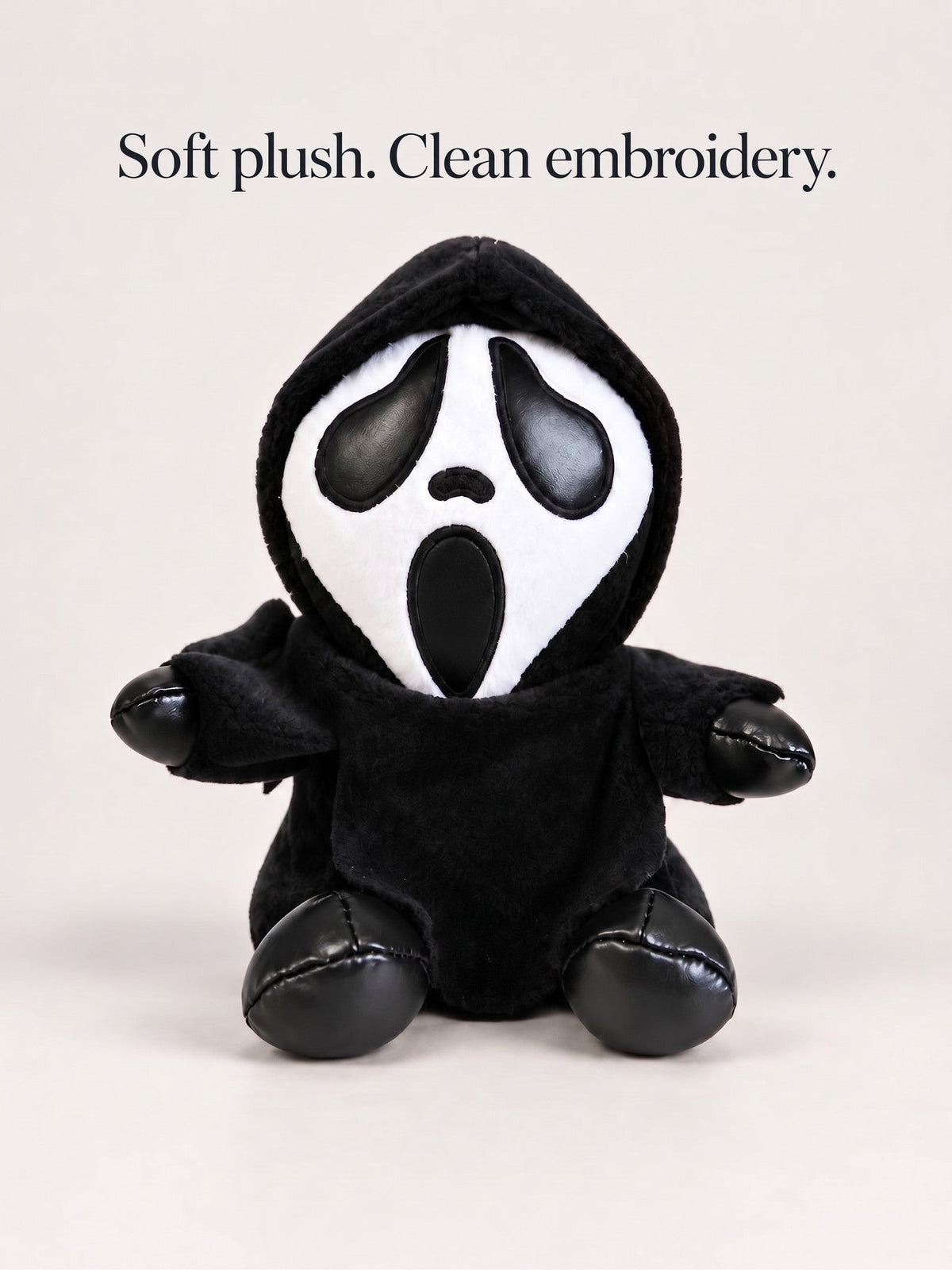 Gloomy Oddboo hooded plush sitting front-facing on an off-white background: black robe, pale scream face with dark teardrop eyes, glossy black paws.