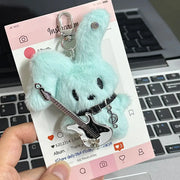 Guitarist Bunny Plush Charm with small guitar, holding a clip, against a background of a phone with social media icons.