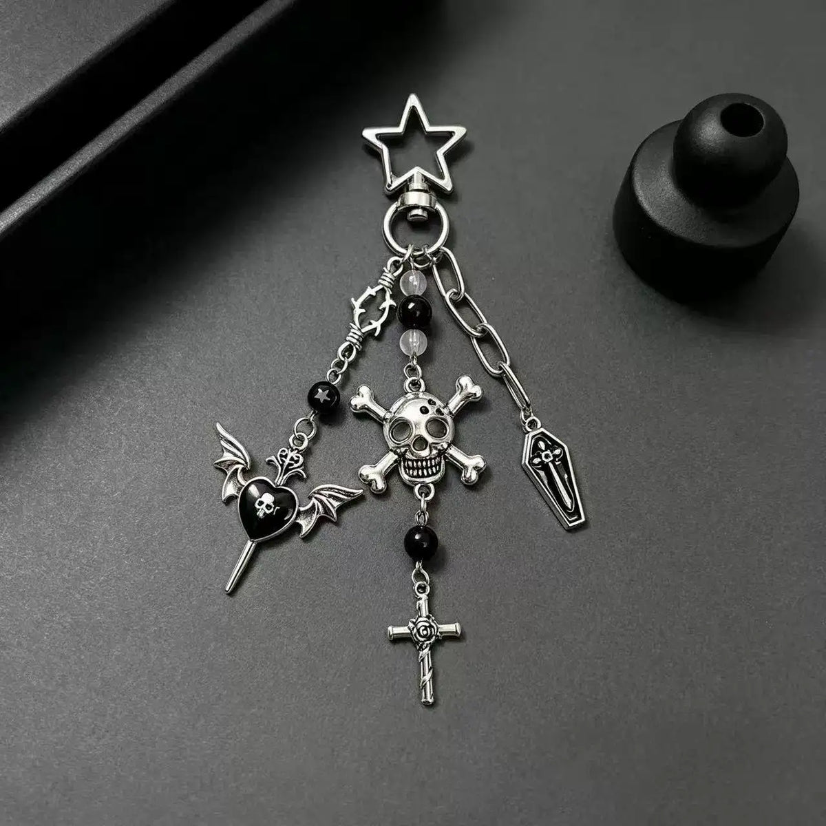 Gothic Skull and Cross Bag Charm featuring skull, cross, and bat designs in silver on a dark background.