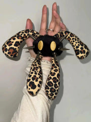 A hand holding a plush keychain shaped like a black spider with leopard-print legs and gold oval eyes, set against a plain light gray background.