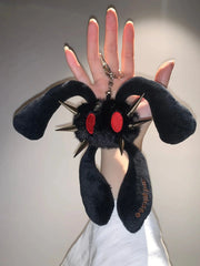 A black plush keychain shaped like a spiky monster with red eyes, held up by a hand against a plain light gray background.