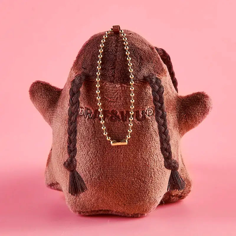 Monster Crew Plush Bag Charm with braids and gold chain on a pink background.