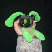 A hand holding a black fuzzy plush monster toy with bright green ears, green eyes, and silver metal spikes against a black background.