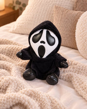 Gloomy Oddboo Buu Evil plush toy with black hood, sitting on cozy blanket in a relaxed setting.