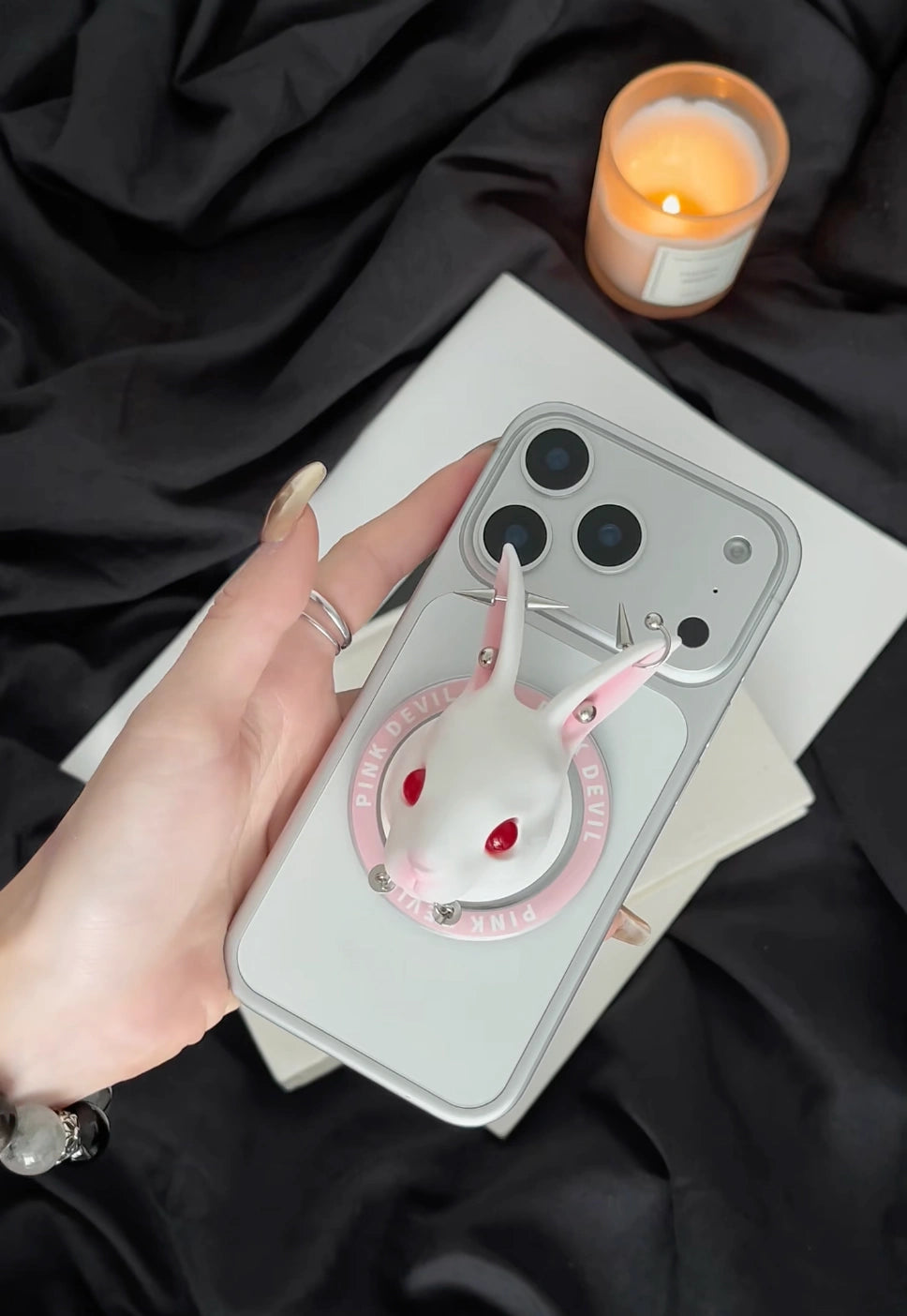 Angry Bunny MagSafe Phone Stand attached to a phone with candle and dark fabric background.