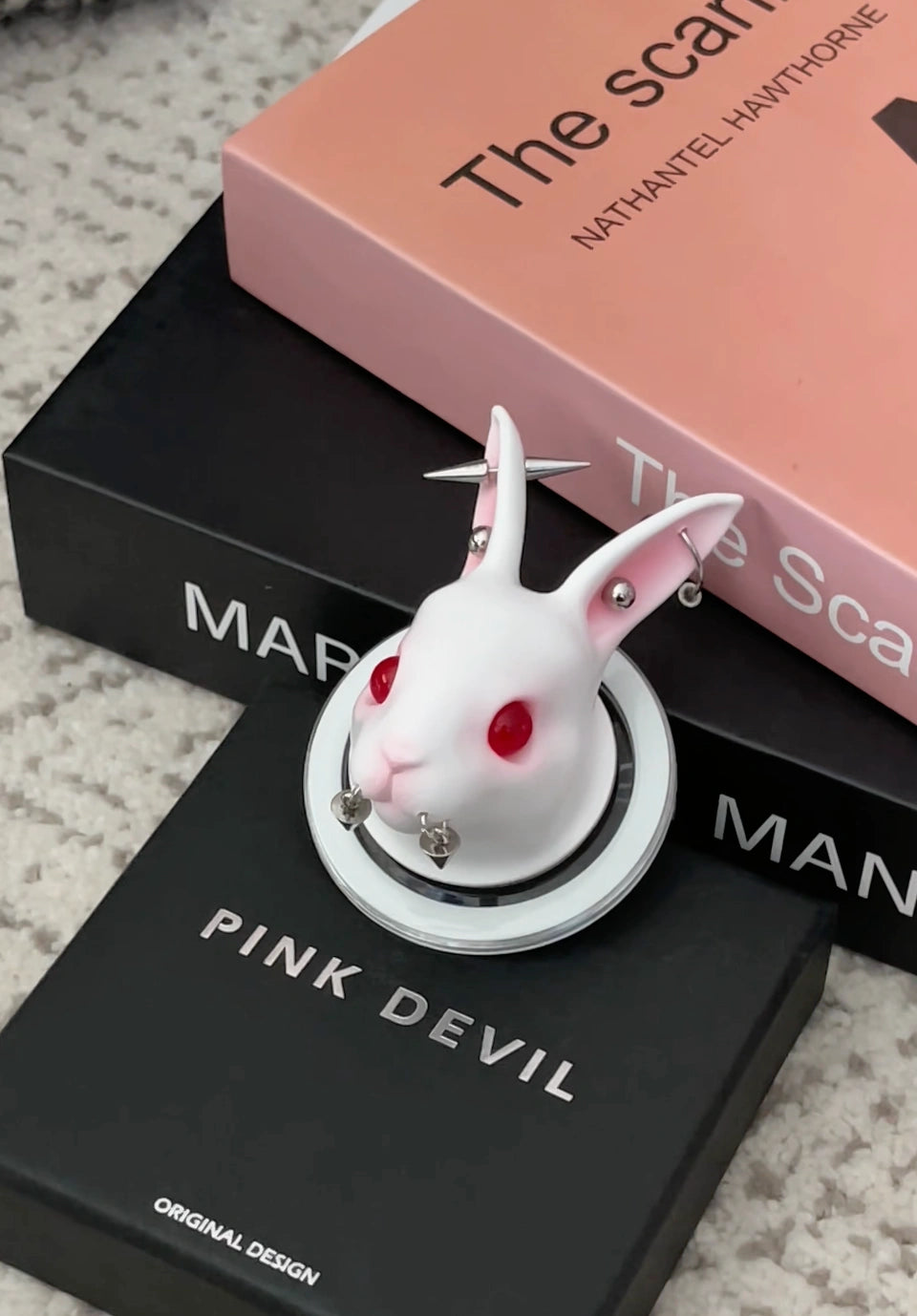 Angry Bunny MagSafe Phone Stand on top of books with a pink cover. Unique rabbit design with red eyes.