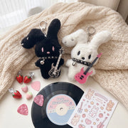 Guitarist Bunny Plush Charm featuring black and white bunny plushies with guitars and accessories on a cozy background.