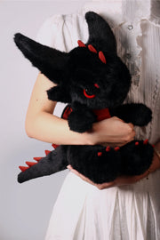 Stuffed dragon Boo, a limited edition plush toy, being held by a person wearing a white dress.