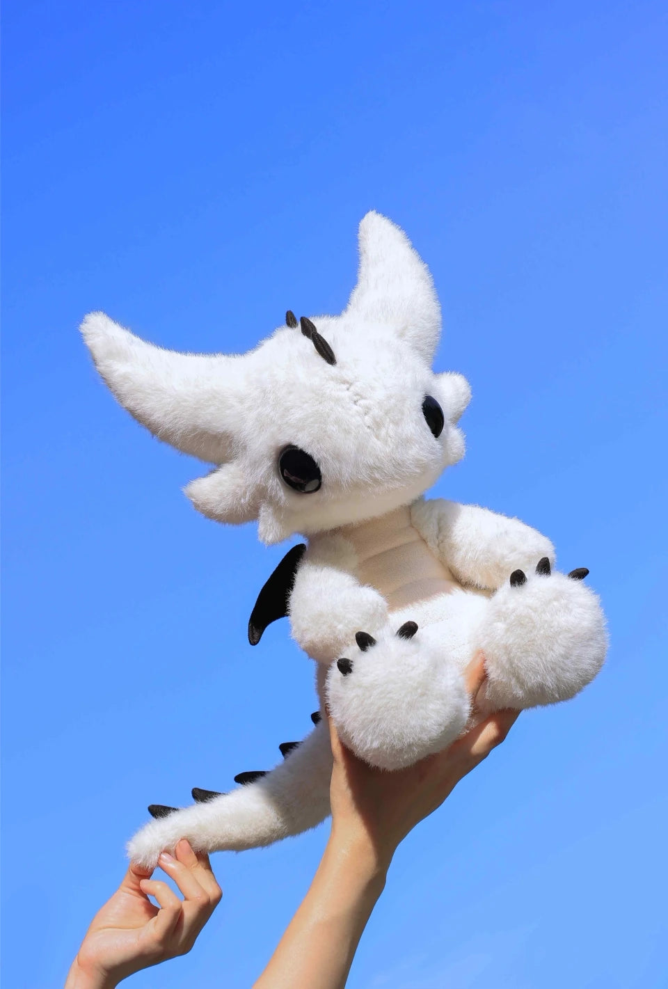 Stuffed dragon Boo plush toy in white being held up against a blue sky, perfect for cuddling and display.