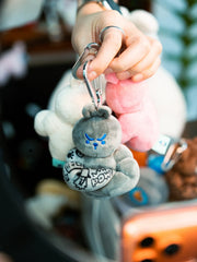Grey fitness bunny plush keychain with POW tattoo sleeve held in hand, kawaii gym rabbit bag charm on metal carabiner