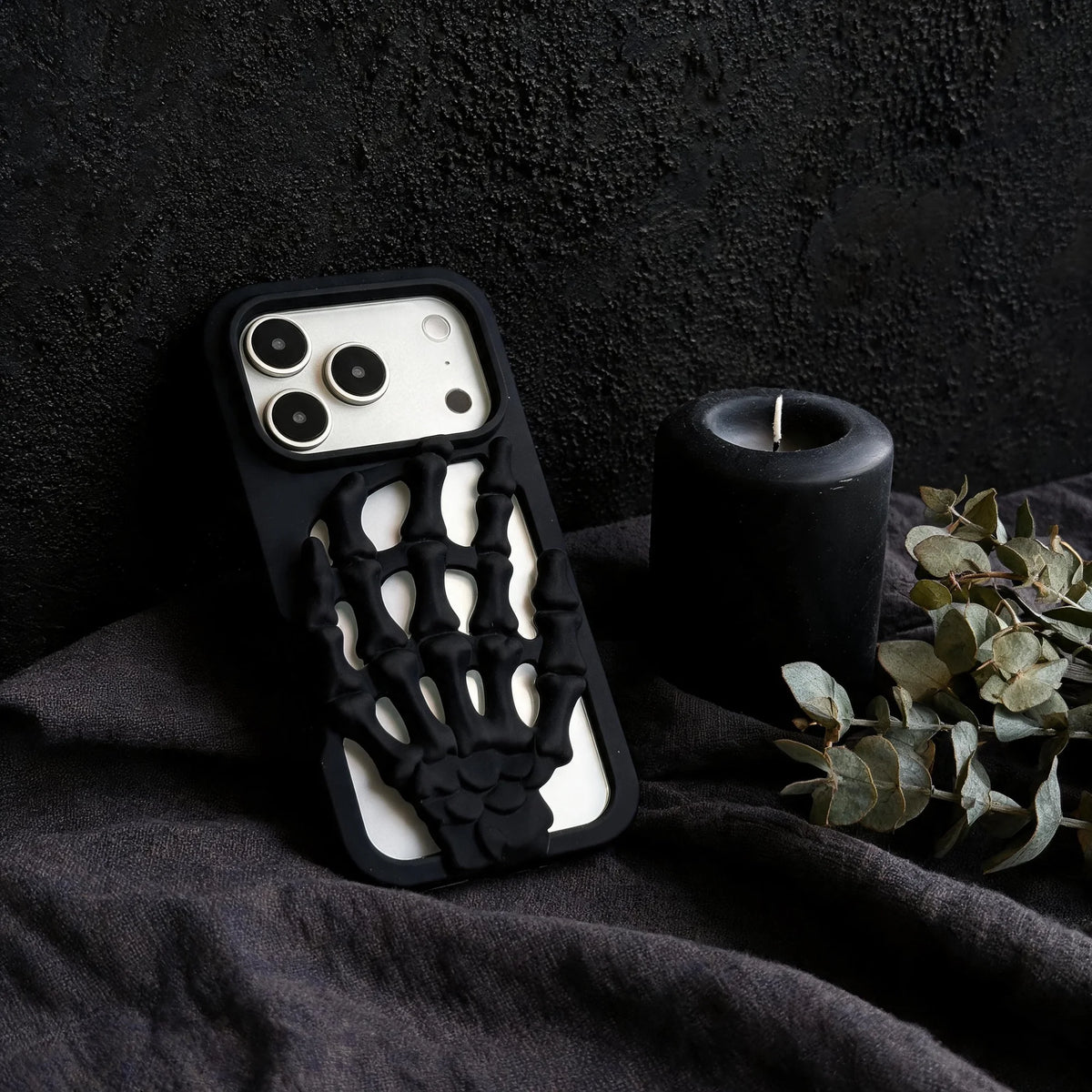 3D Skeleton Hand Gothic Phone Cover with a sculpted skeleton hand design, resting next to a candle and greenery.