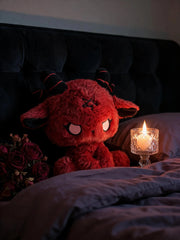 Dark Envoy Gothic Cute Plush Doll - Buu Evil resting on a bed next to a candle and roses, creating a cozy gothic atmosphere.