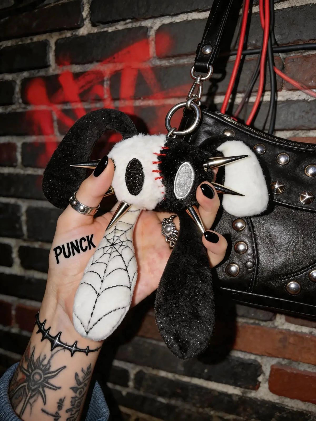 Punk Rabbit plush bag charm and keychain with edgy details and four ears in a hand against a brick wall.