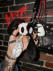 Punk Rabbit plush bag charm and keychain with edgy details and four ears in a hand against a brick wall.