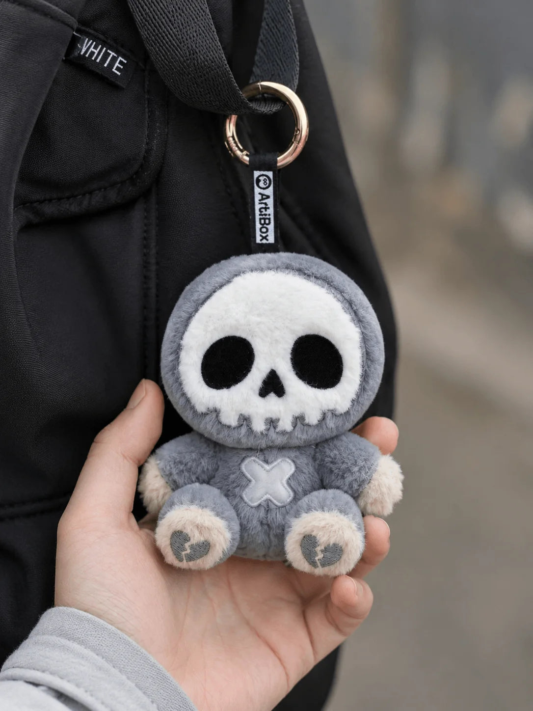 Little Angu plush charm hanging from a bag, showcasing its cute skull design and stitched features.