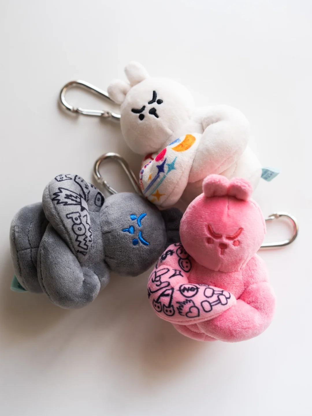 Three muscle bunny plush keychains in white grey and pink flat lay with silver carabiners, tattoo sleeve fitness gift