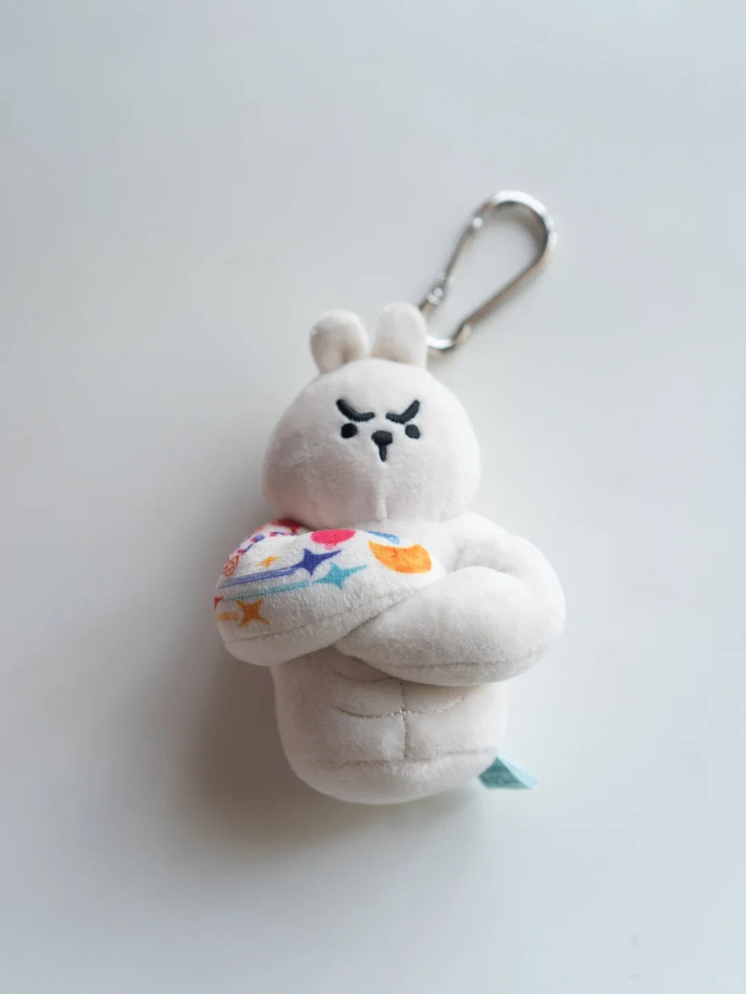 Bunny plush bag charm with a round face and long ears, featuring a six-pack and colorful donut design.